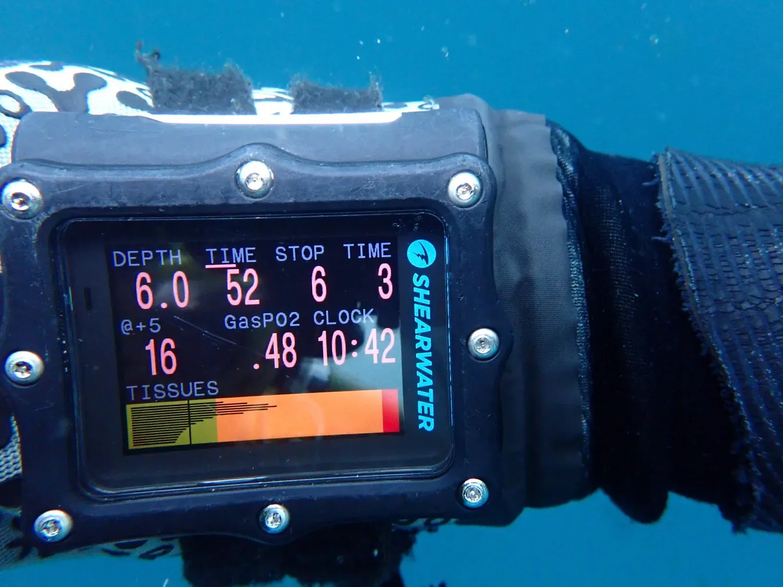 A Shearwater dive computer worn underwater, showing depth, stop depth, gas PO2 and a bar graph of estimated tissue loading